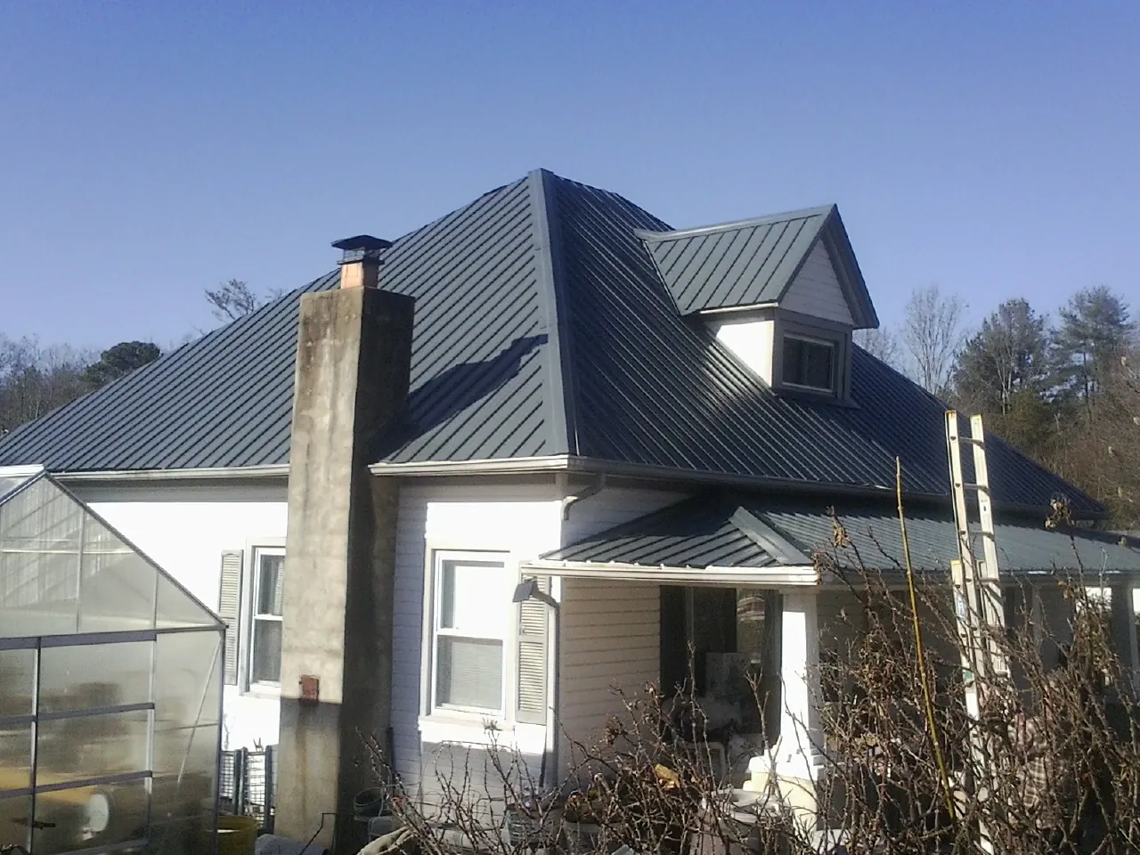 Dark blue standing seam metal roof on a white farmhouse with dormer — Slate & Tile Roof Repair by Roofing Brothers in New Braunfels