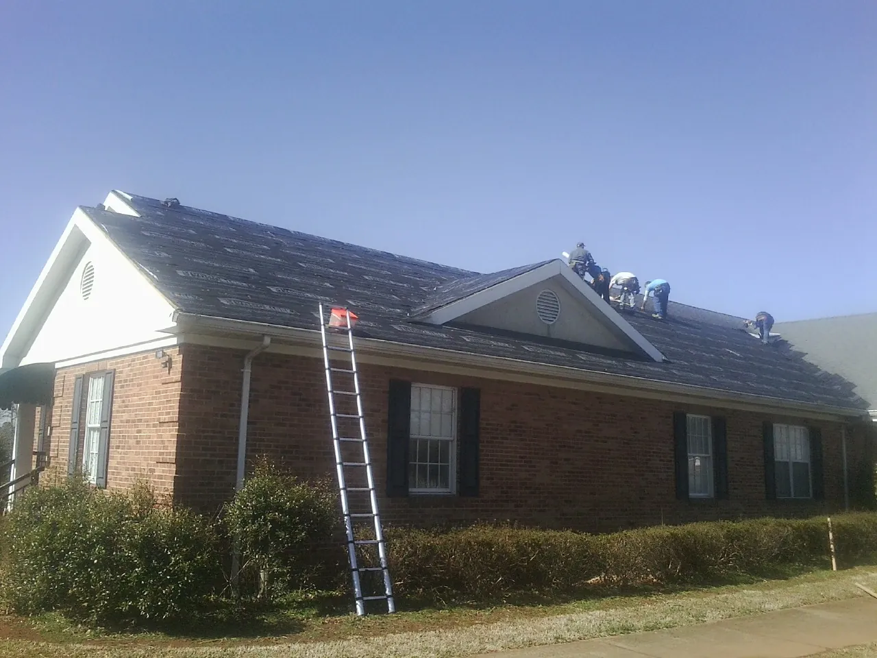 Crew tearing shingles off a brick ranch roof with a ladder set — Emergency Roof Repair work by our crew in New Braunfels