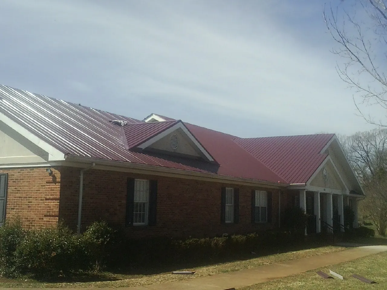 Red metal roof with gabled entries on a long brick building, from a Hail Damage Roof Repair job in New Braunfels