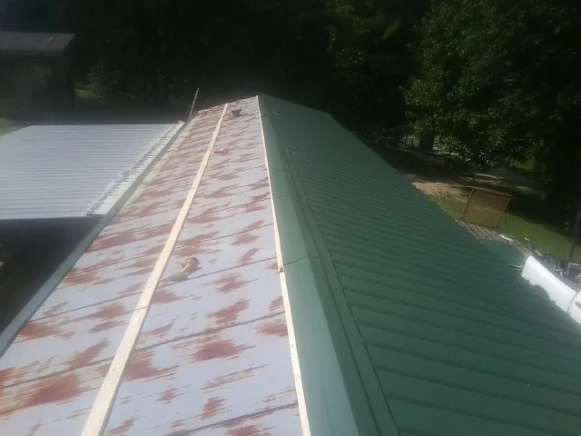 Old rusted panels beside newly installed green metal roofing — Wind Damage Roof Repair by Roofing Brothers in New Braunfels