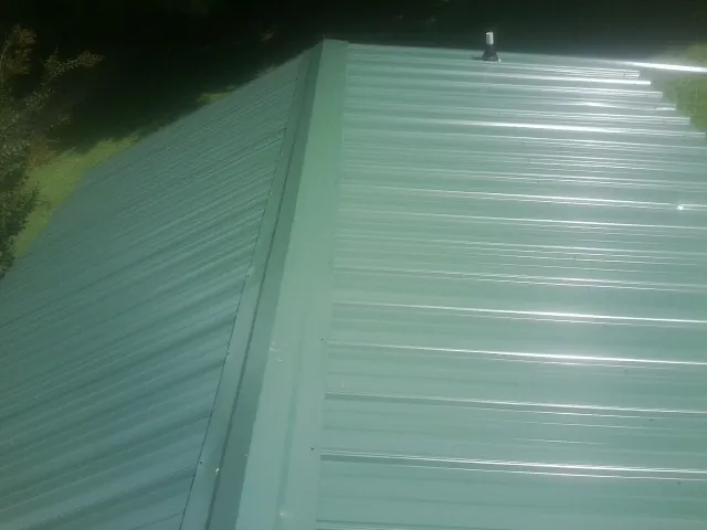 New green metal panels meeting at the ridge of a roof — Flat Roof Repair work by our crew in New Braunfels