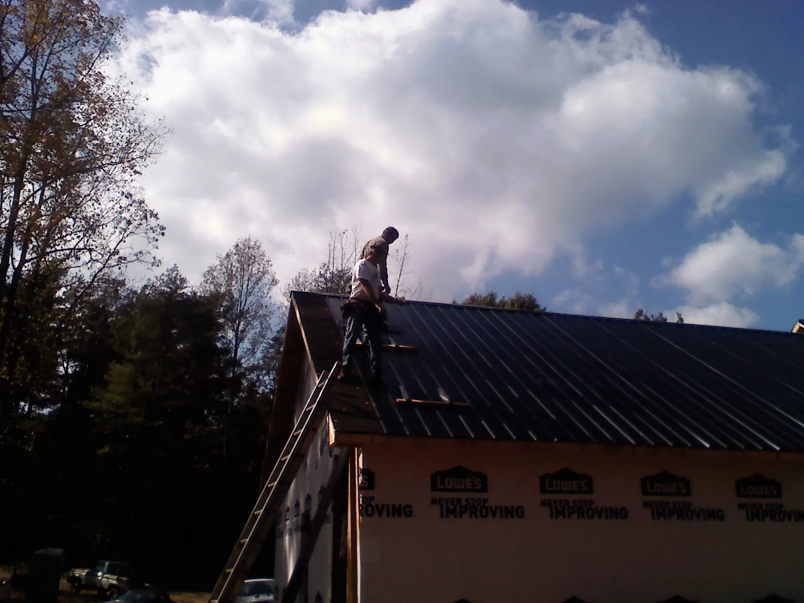 Roofer fastening dark metal panels high against a cloudy sky, from a Roof Inspection job in New Braunfels