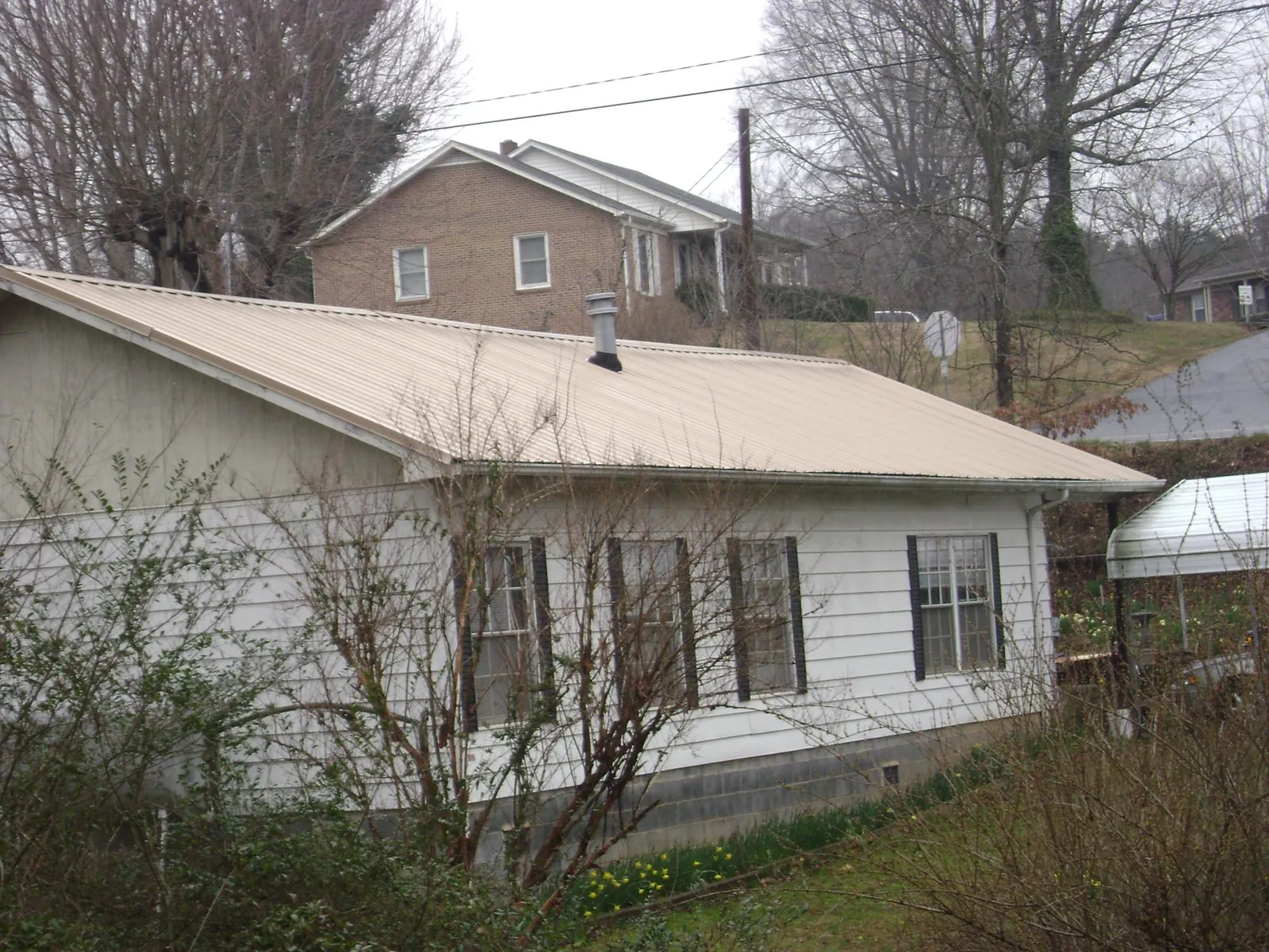 Tan metal roof on a white sided house set into a hillside — Commercial Roofing by Roofing Brothers in New Braunfels